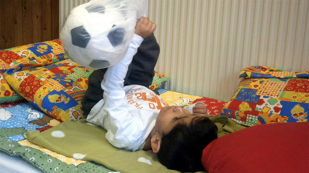 Kind liegt auf Decken und spielt mit Ball