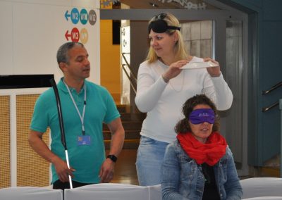 Workshop 7 von Juan Ruiz. Er steht neben zwei Workshopteilnehmerinnen, welche gerade einen Selbstversuch mit einer Simulationsbrille durchführen.