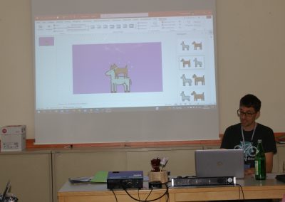 Workshop 9 von Leonhard Matejka. Er präsentiert METACOM9 auf seinem Laptop. Hinter ihm auf der Leinwand können die Teilnehmer*innen sehen, wie er Symbole kombiniert.